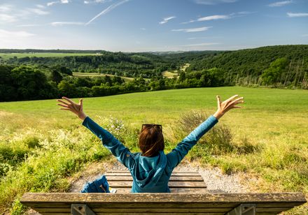 Vrouw zit op een ligstoel in de natuur en strekt haar armen uit