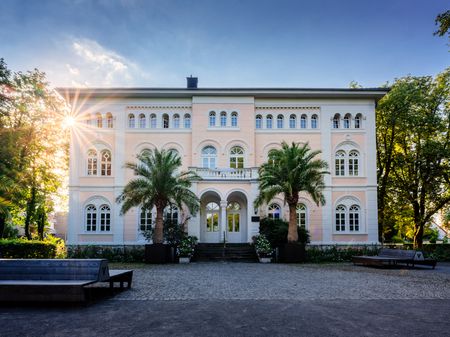 Villa met twee palmbomen ervoor, links de zon