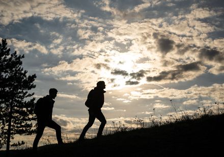 Twee mensen lopen de berg af; je ziet hun silhouetten